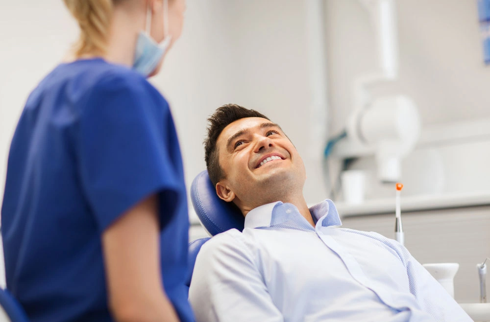 Happy men smiling on dental chair after getting teeth whitening treatment